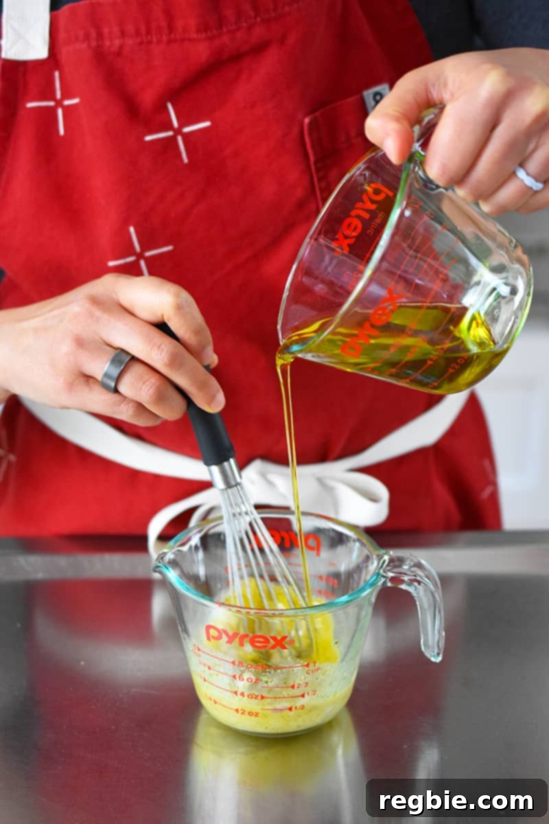 Whole30 Keto Paleo Asparagus Mimosa 15 Someone in a red apron is whisking extra virgin olive oil into a measuring cup with vinaigrette ingredients.