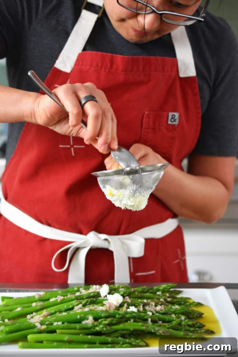 Whole30 Keto Paleo Asparagus Mimosa 17 A woman in a red apron is pressing egg whites through a small sieve on top of cooked asparagus