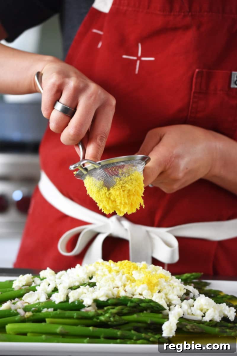 Whole30 Keto Paleo Asparagus Mimosa 4 Someone in a red apron is pushing hard cooked egg yolks though a small sieve to make asparagus mimosa.