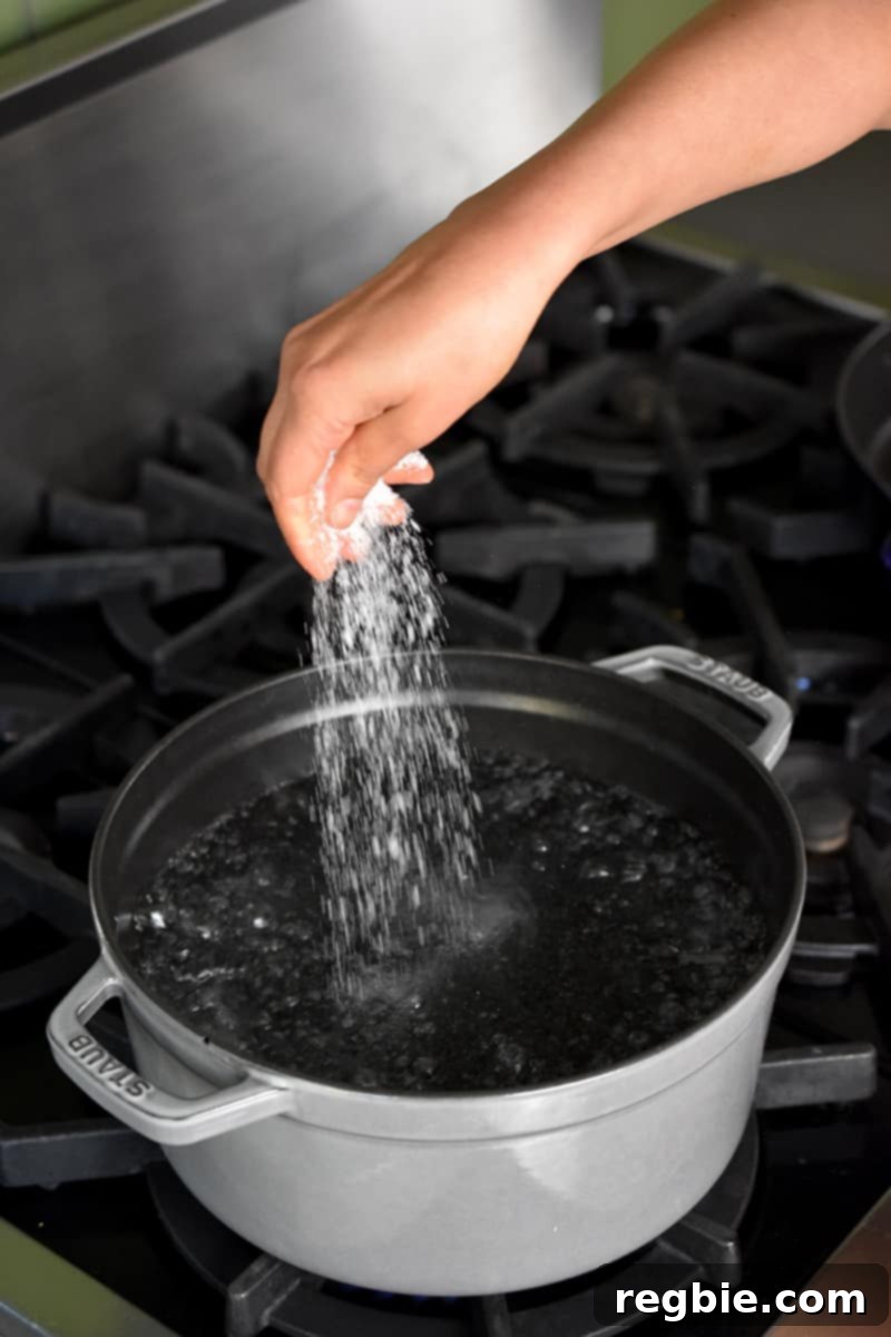 Whole30 Keto Paleo Asparagus Mimosa 8 A hand is adding a large pinch of Diamond Crystal kosher salt into a large gray pot filled with boiling water.