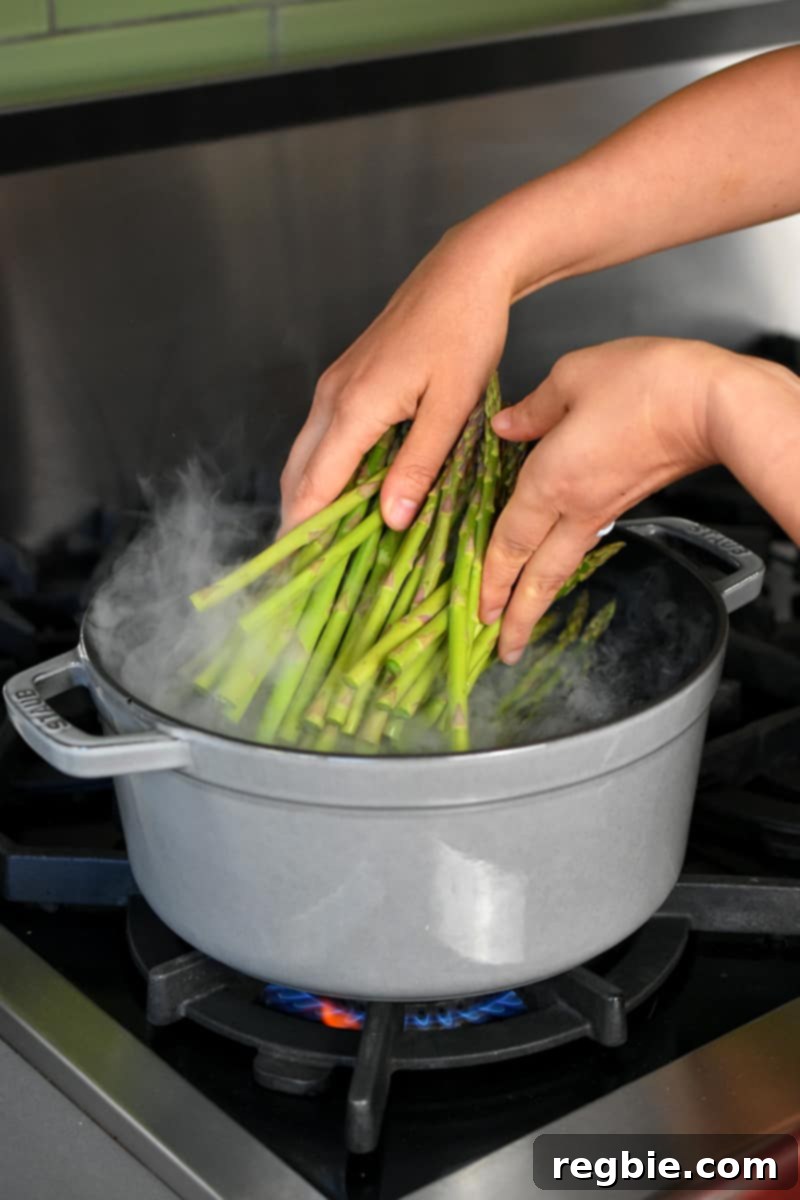 Whole30 Keto Paleo Asparagus Mimosa 9 Two hands adding asparagus to a gray stock pot filled with boiling water.