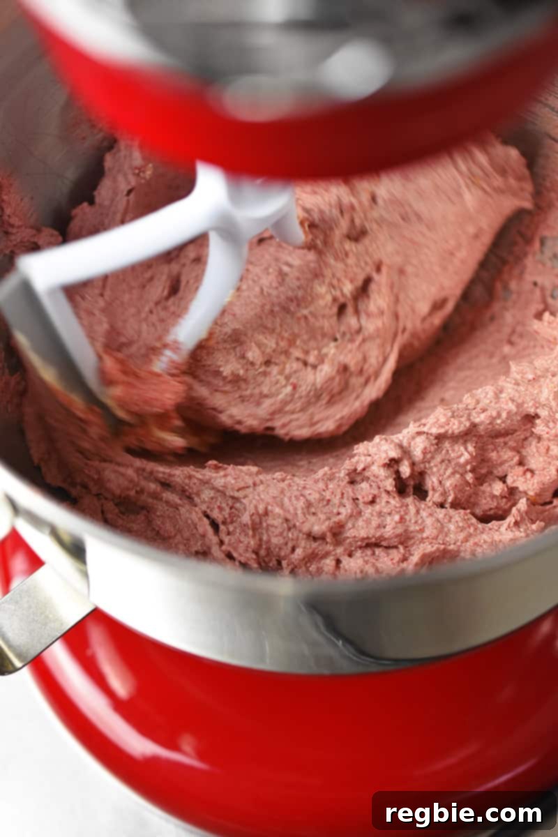 An overhead view captures the fully mixed strawberry muffin batter, a delightful pink hue, resting within the bowl of a stand mixer, ready for the next steps.