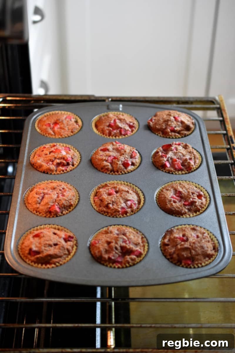 A muffin pan, laden with perfectly golden-brown strawberry muffins, sits invitingly inside an open oven, showcasing their baked readiness.