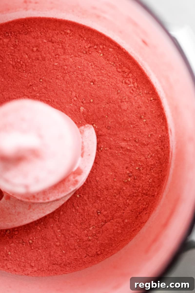 An overhead view of an open food processor bowl reveals a perfectly fine, pink powder, created from blitzed freeze-dried strawberries.