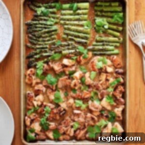 An overhead shot of sheet pan chicken and asparagus on a wooden table, next to bowls of cauliflower rice, plates, and forks.