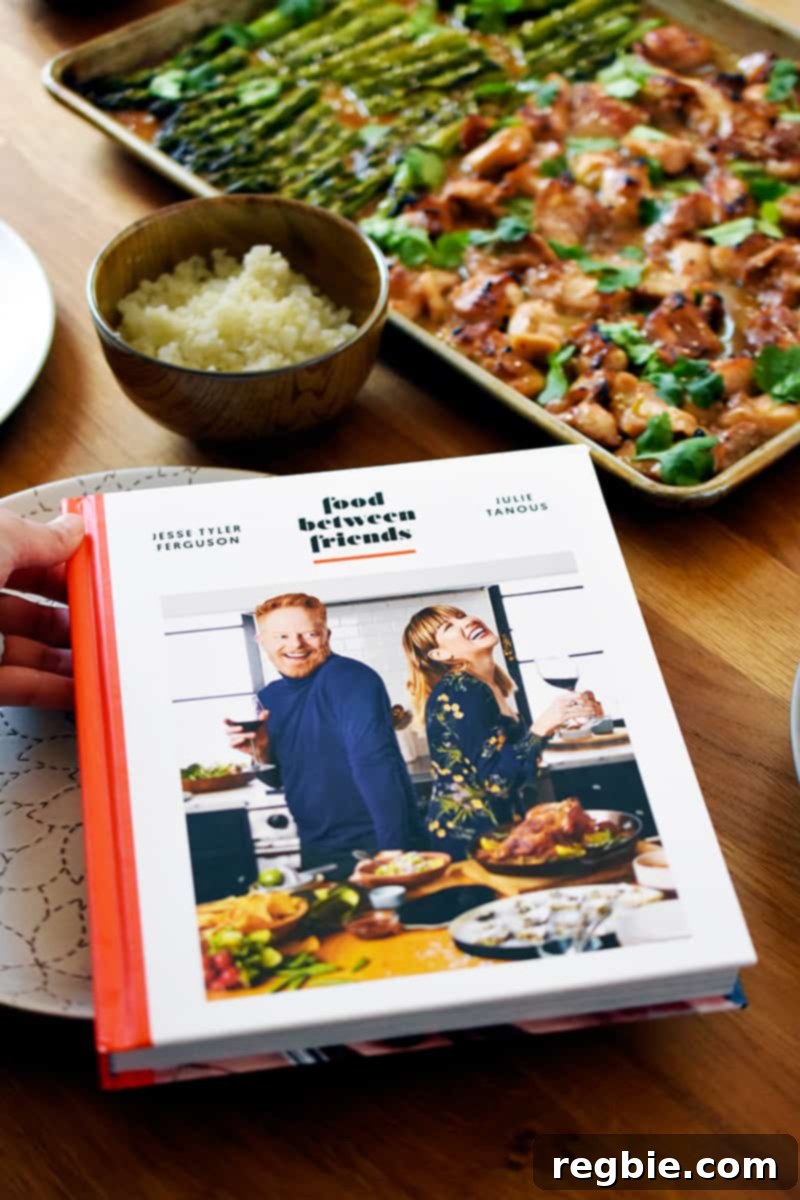 Simple Sheet Pan Chicken & Asparagus: Paleo Perfection 3 A hardcover copy of the 'Food Between Friends' cookbook rests beside a serving of Sheet Pan Chicken and Asparagus and a bowl of fluffy cauliflower rice, highlighting the perfect meal pairing.