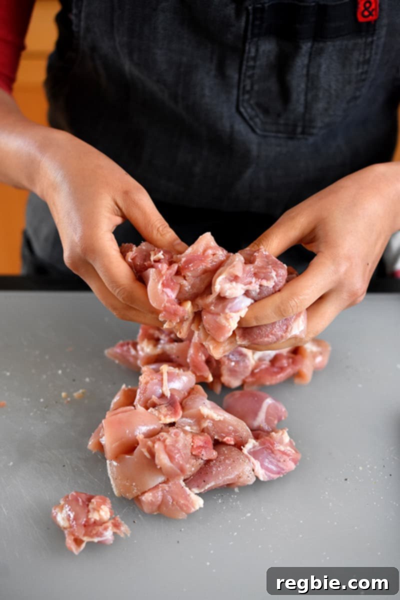 Simple Sheet Pan Chicken & Asparagus: Paleo Perfection 7 Two hands are actively tossing raw chicken cubes with a generous seasoning of salt and pepper on a plastic cutting board, ensuring every piece is coated before marinating.