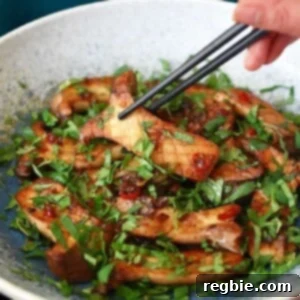 A pair of black chopsticks is picking up a piece of King trumpet mushrooms with Thai Chili peppers and lime from a light blue bowl.