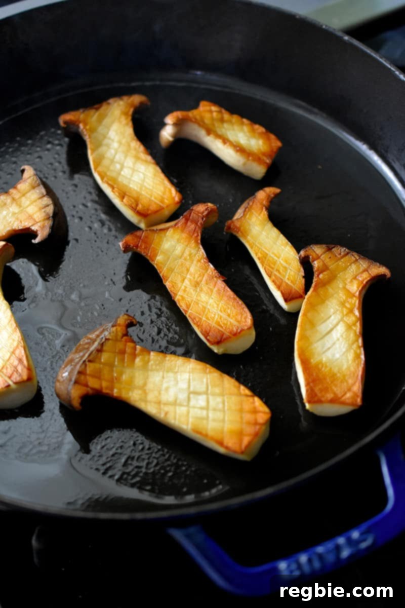 Overhead shot of browned king oyster mushrooms outside up in a cast iron skillet. The mushrooms have a crisscross pattern on the cut surface