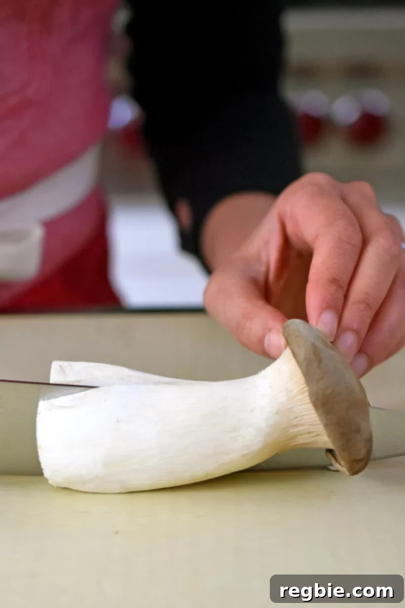 Someone using a chef's knife to slice a king oyster mushroom in half lengthwise.