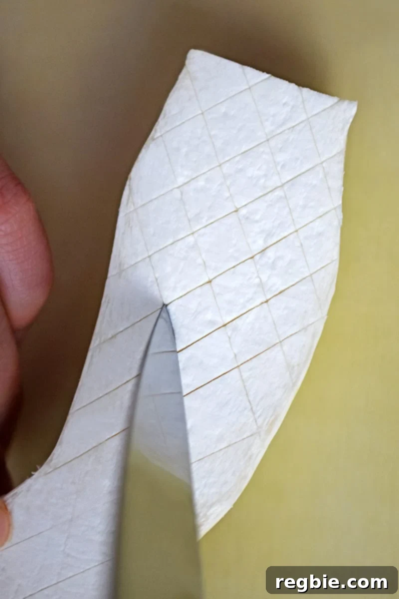 A sharp paring knife is cutting a shallow criss-cross pattern on the cut side of the king oyster mushroom