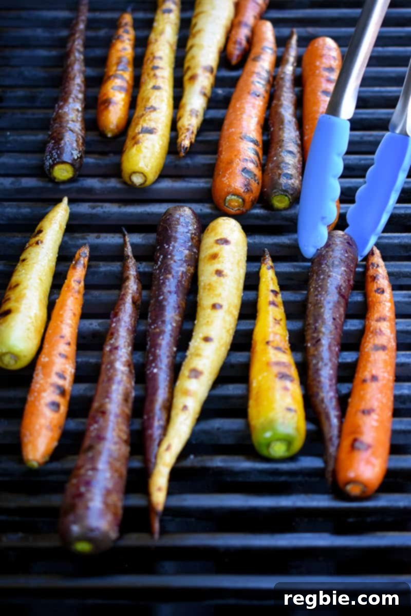 An overhead shot of rainbow colored carrots with char marks on a gas grill