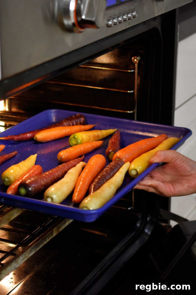 Someone putting a blue rimmed baking sheet filled with rainbow colored carrots into an open oven.