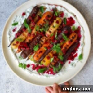 A hand is holding a round platter filled with grilled carrots with herby coconut yogurt and spicy beet vinaigrette