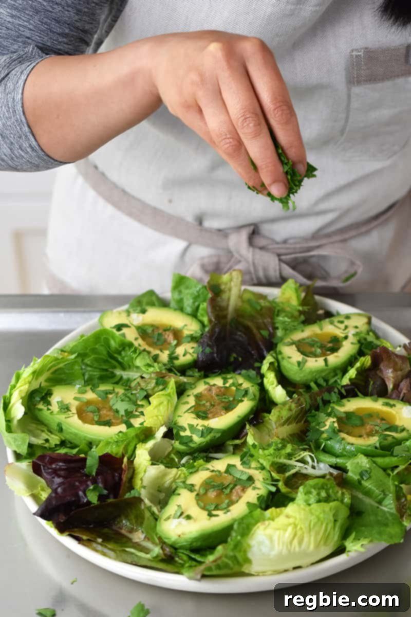 Irresistible Umami Avocado Salad with Garlic Anchovy Vinaigrette 16 A person in a white apron is sprinkling fresh herbs on the avocado salad.