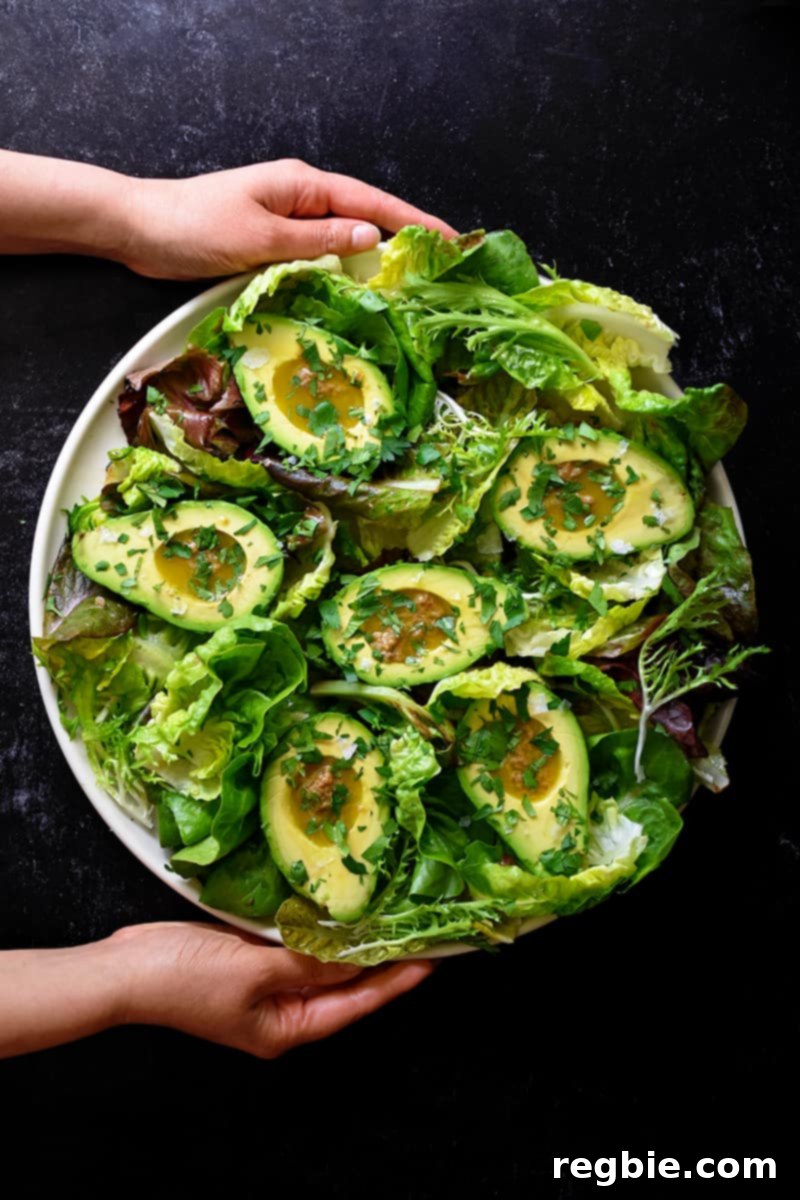 Irresistible Umami Avocado Salad with Garlic Anchovy Vinaigrette 4 An overhead shot of two hands holding a round platter filled with avocado salad and garlic anchovy vinaigrette