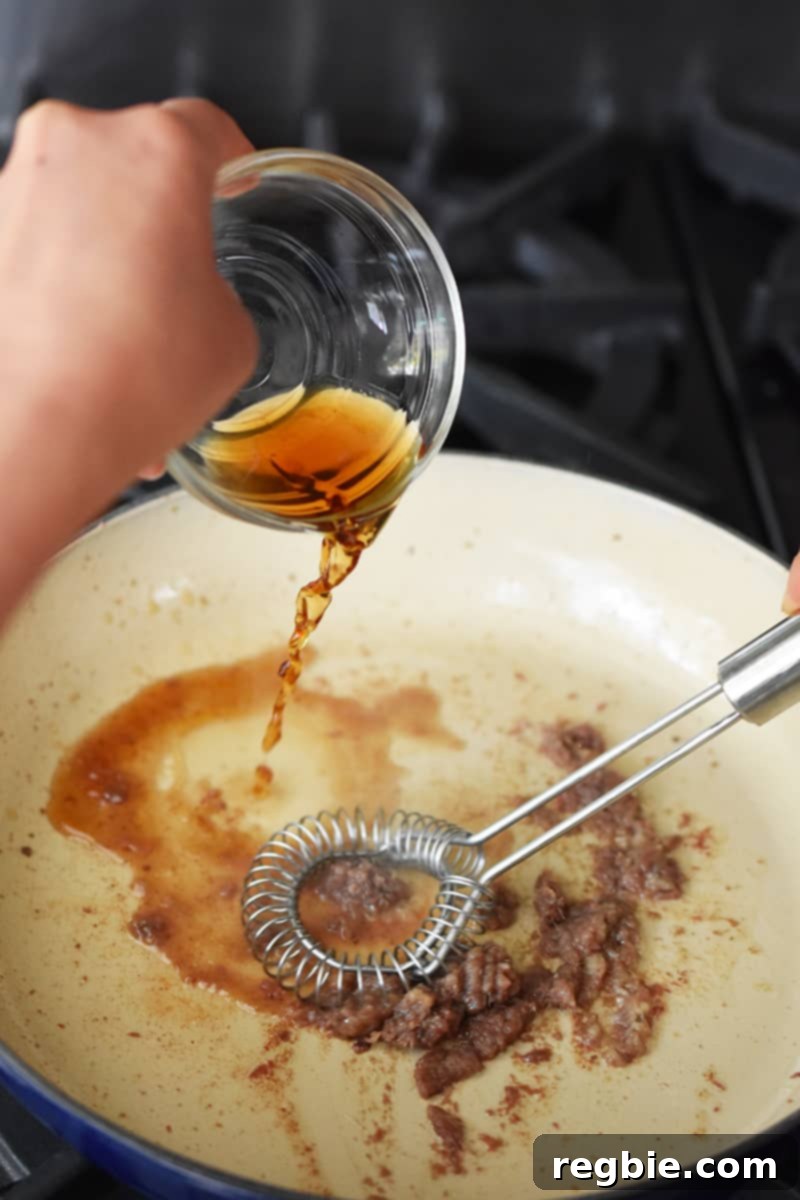 Irresistible Umami Avocado Salad with Garlic Anchovy Vinaigrette 8 A hand is adding a bowl of sherry vinegar into a ceramic cast iron skillet filled with minced anchovies and garlic