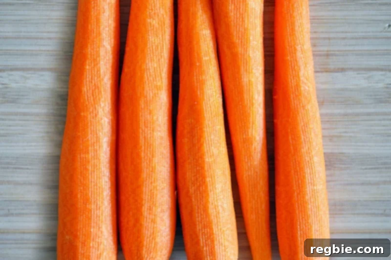 An overhead shot of five peeled carrots on a wooden cutting board, ready for slicing.