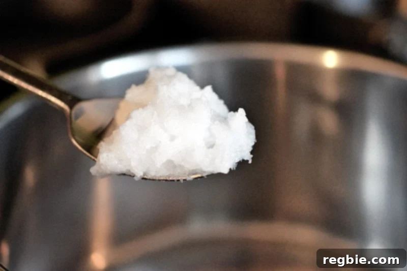 Adding a spoonful of coconut oil to a saucepan over medium heat.