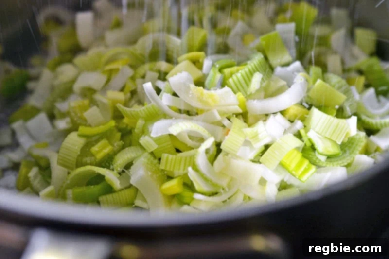 Sprinkling salt on sliced leeks in a saucepan for Carrot Cardamom Soup.