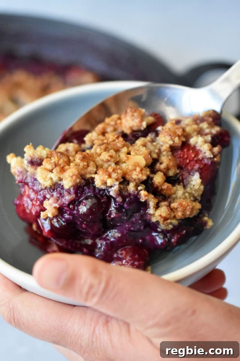 A close-up of someone scooping gluten-free berry crisp into a shallow bowl.