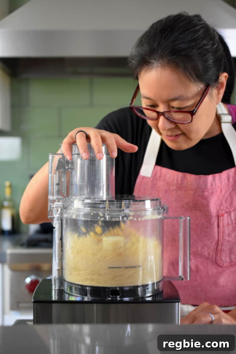 An Asian woman is pulsing a berry crisp topping in a food processor.