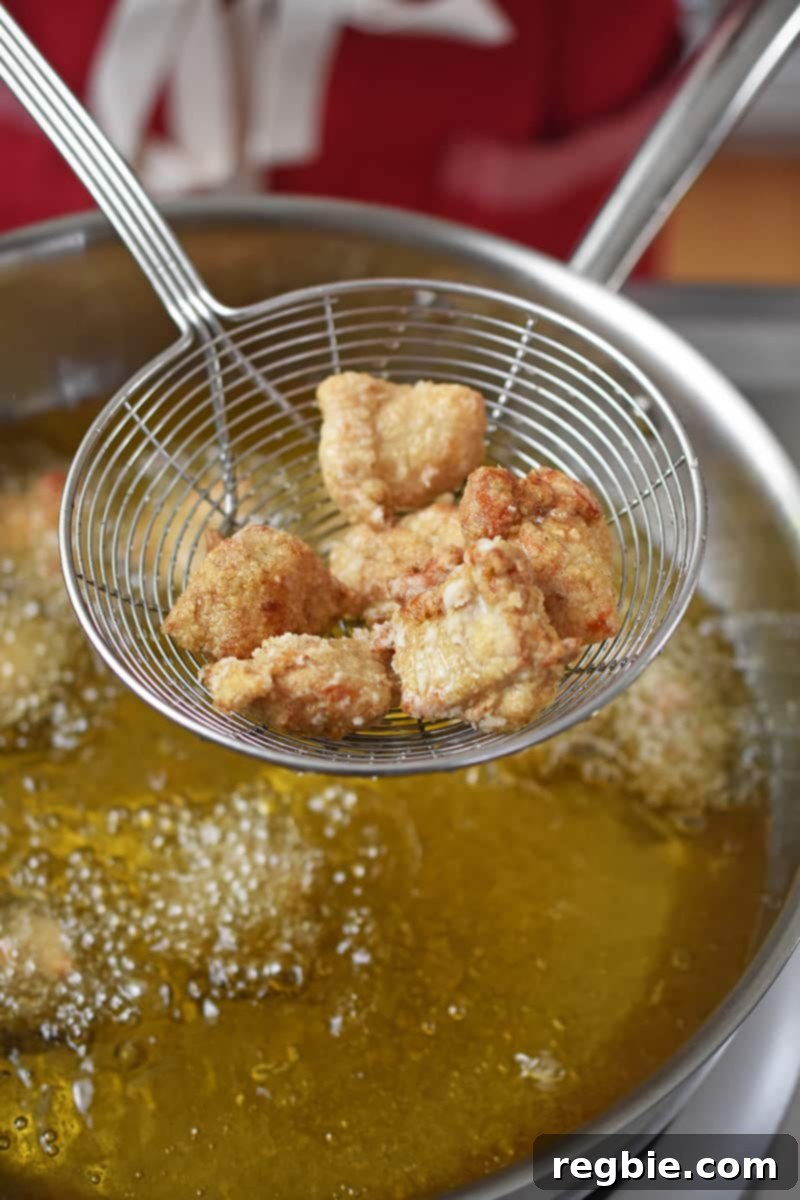 An overhead shot of a metal strainer removing Taiwanese popcorn chicken from a pot filled with hot oil.
