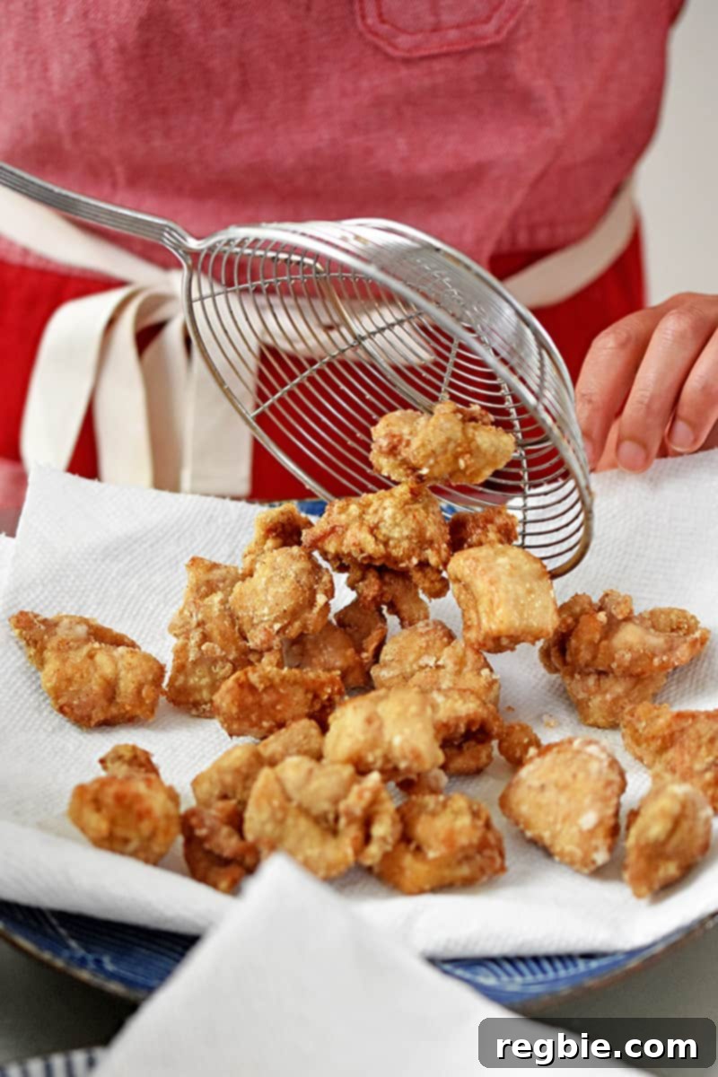 Transferring the deep fried Taiwanese fried chicken onto a paper towel lined plate.
