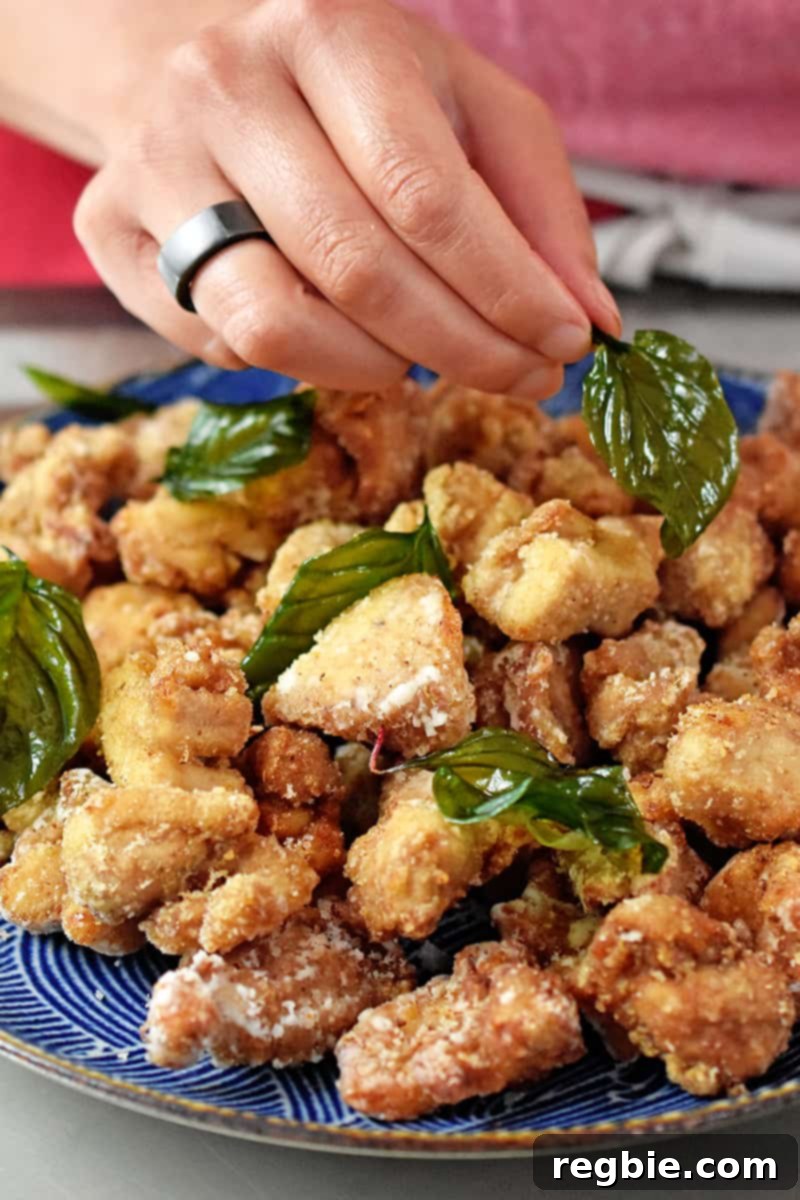 A hand is garnishing a platter of Taiwanese popcorn chicken with fried basil.