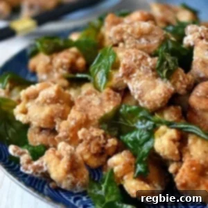 A side shot of a blue plate filled with gluten free and paleo Taiwanese popcorn chicken and fried basil