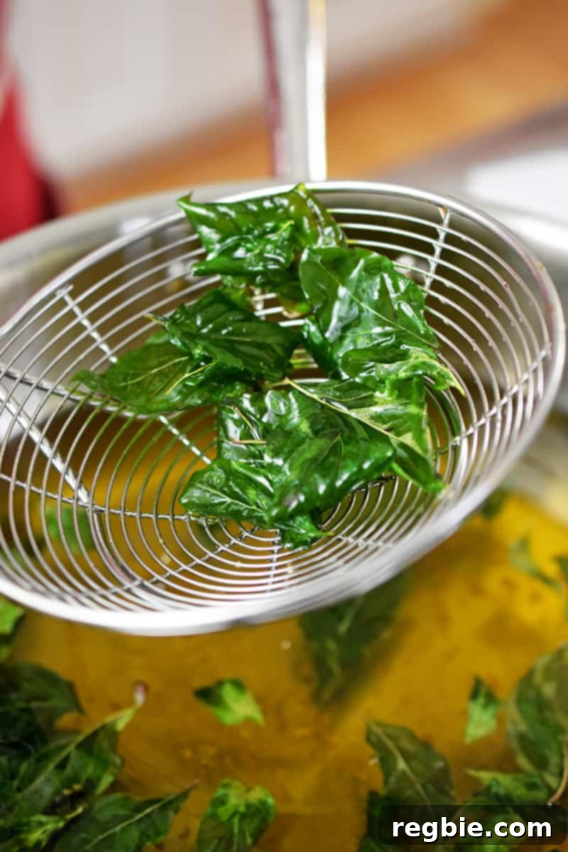 A metal strainer has fried basil in it.