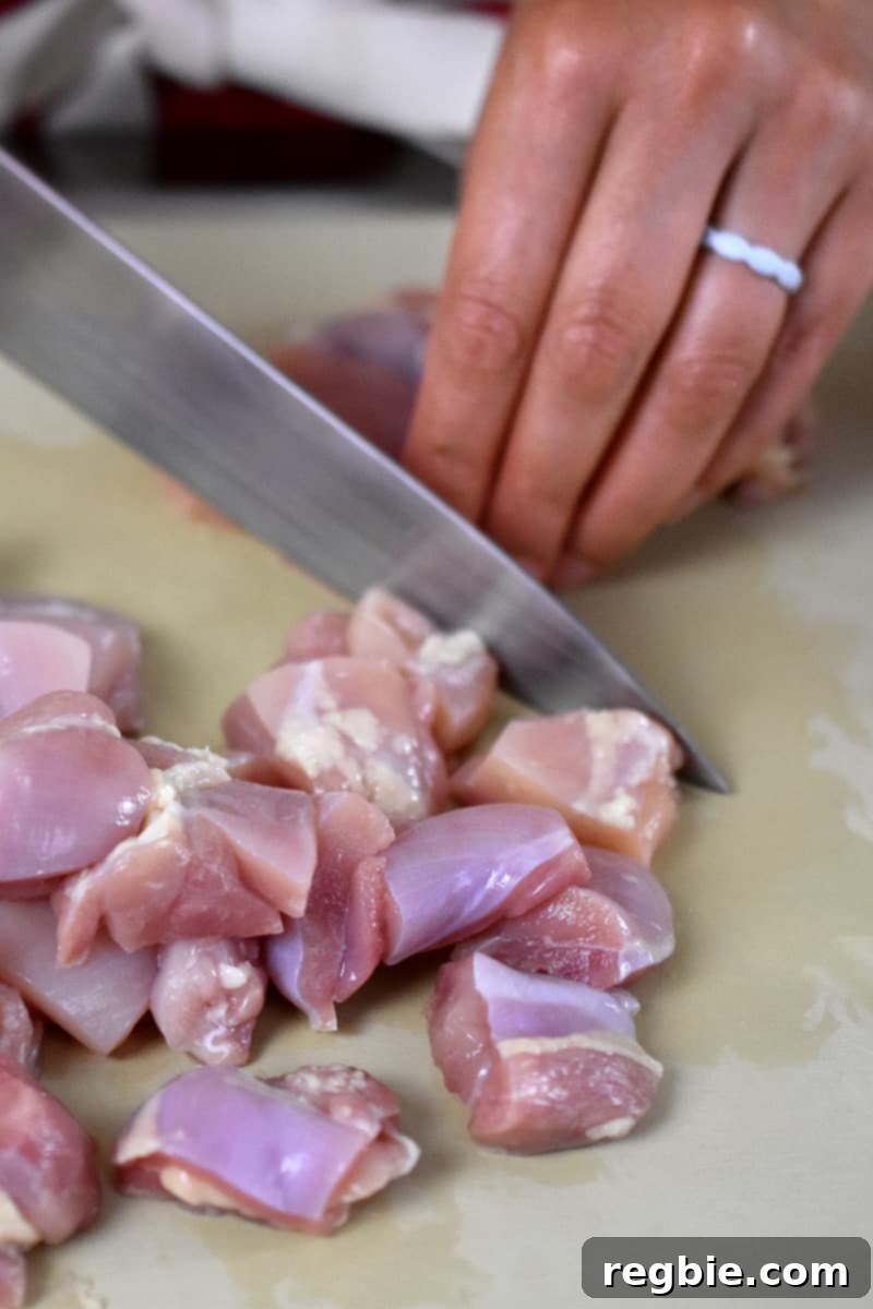 Someone is cutting up boneless, skinless chicken thighs into bite-sized pieces