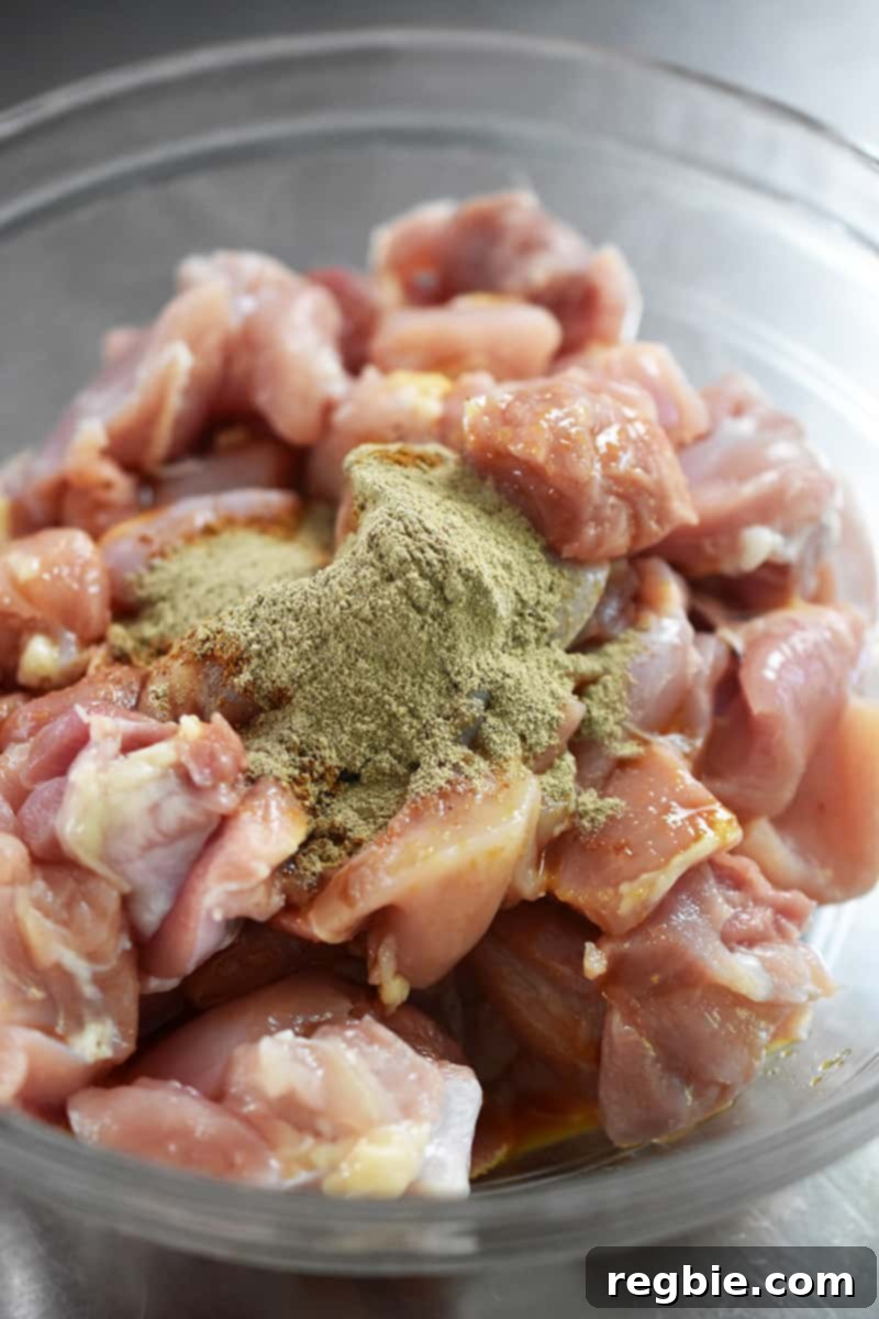 A bowl of cubed, marinated chicken with five spice powder and ground white pepper on top.