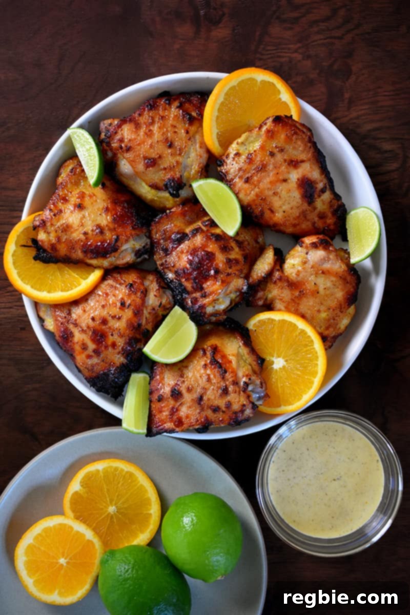 An overhead shot of mojo chicken with golden brown skin in a bowl next to a bowl of dipping sauce.