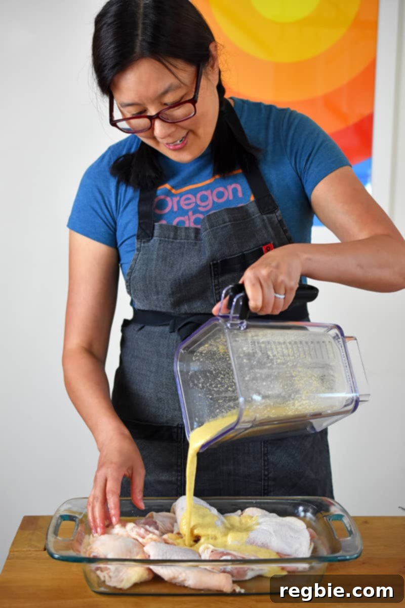 An Asian woman is pouring mojo sauce on chicken thighs in a glass container.