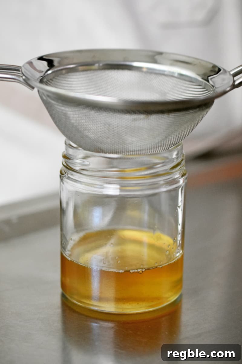 Master Crispy Microwave Bacon: Clean and Waste-Free 11 A side shot of a small glass jar filled with golden bacon drippings. The jar has a fine mesh sieve on top.