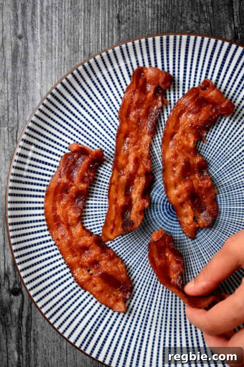 Master Crispy Microwave Bacon: Clean and Waste-Free 3 A hand grabbing a piece of crispy microwave bacon from a blue and white plate