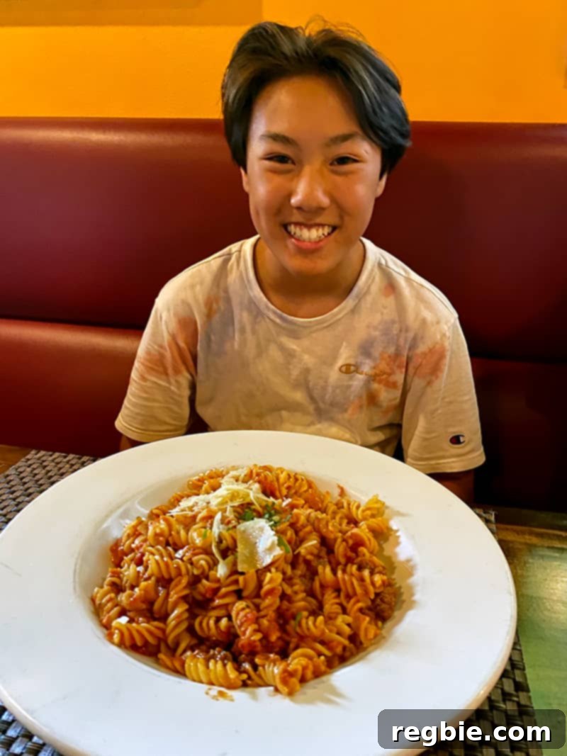 A smiling Asian teenager with a big bowl of gluten-free pasta from Pueo's Osteria on the Big Island