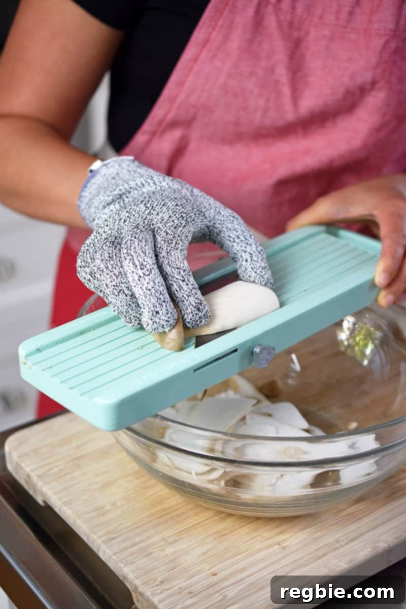 Someone wearing cut-resistant gloves is using a Japanese mandolin to shave king oyster mushrooms.