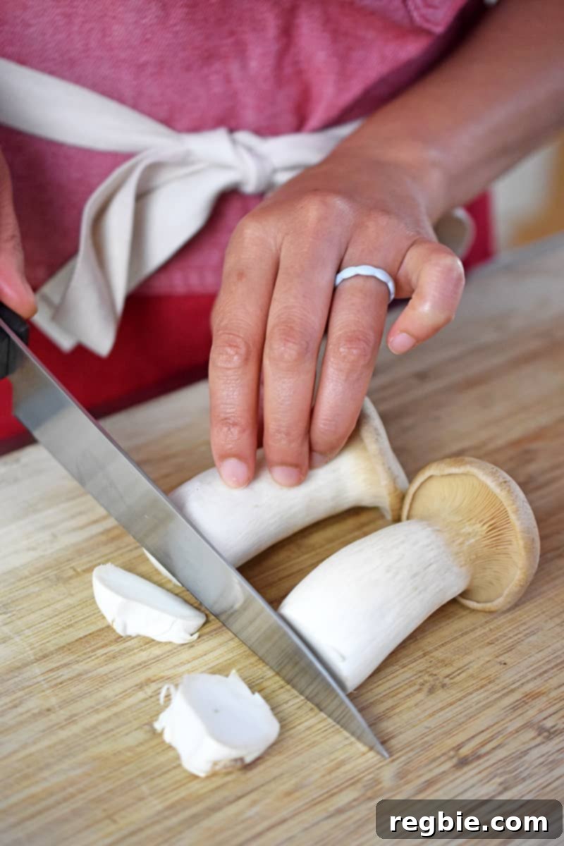 Someone in a red apron is cutting the bottoms off of two king oyster mushrooms.