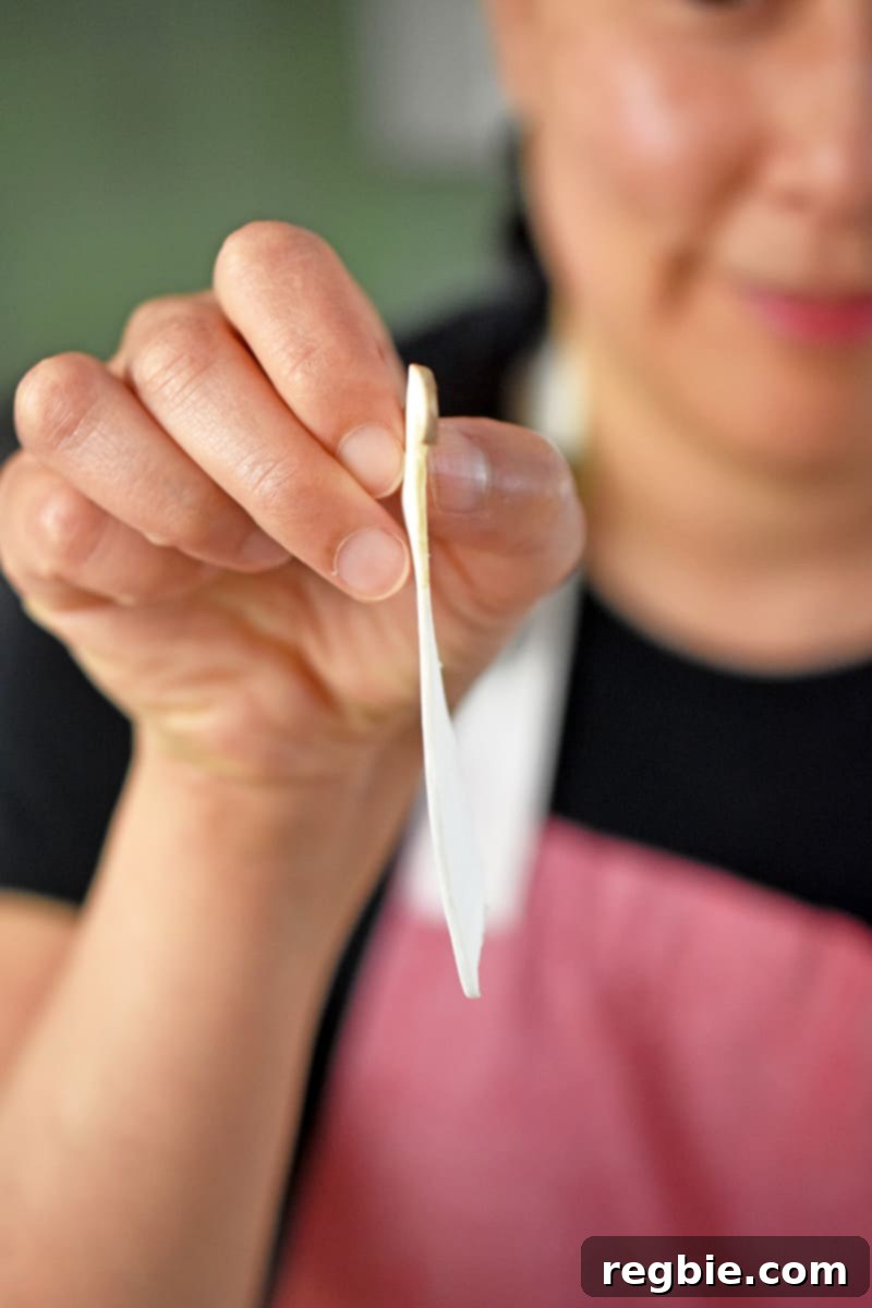 A woman in a red apron is holding up a paper thin slice of king oyster mushroom.