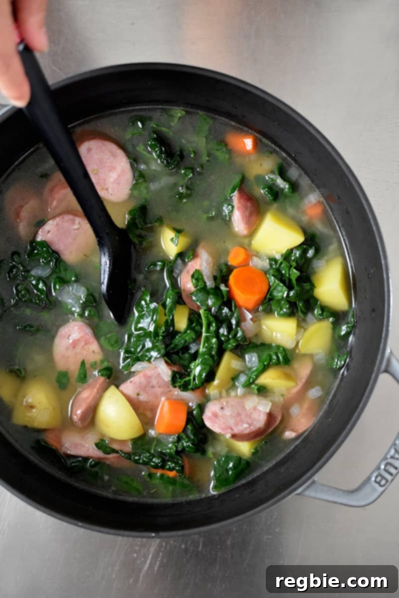 Overhead shot of all ingredients for kale and sausage soup in a pot, ready to simmer on the stovetop.