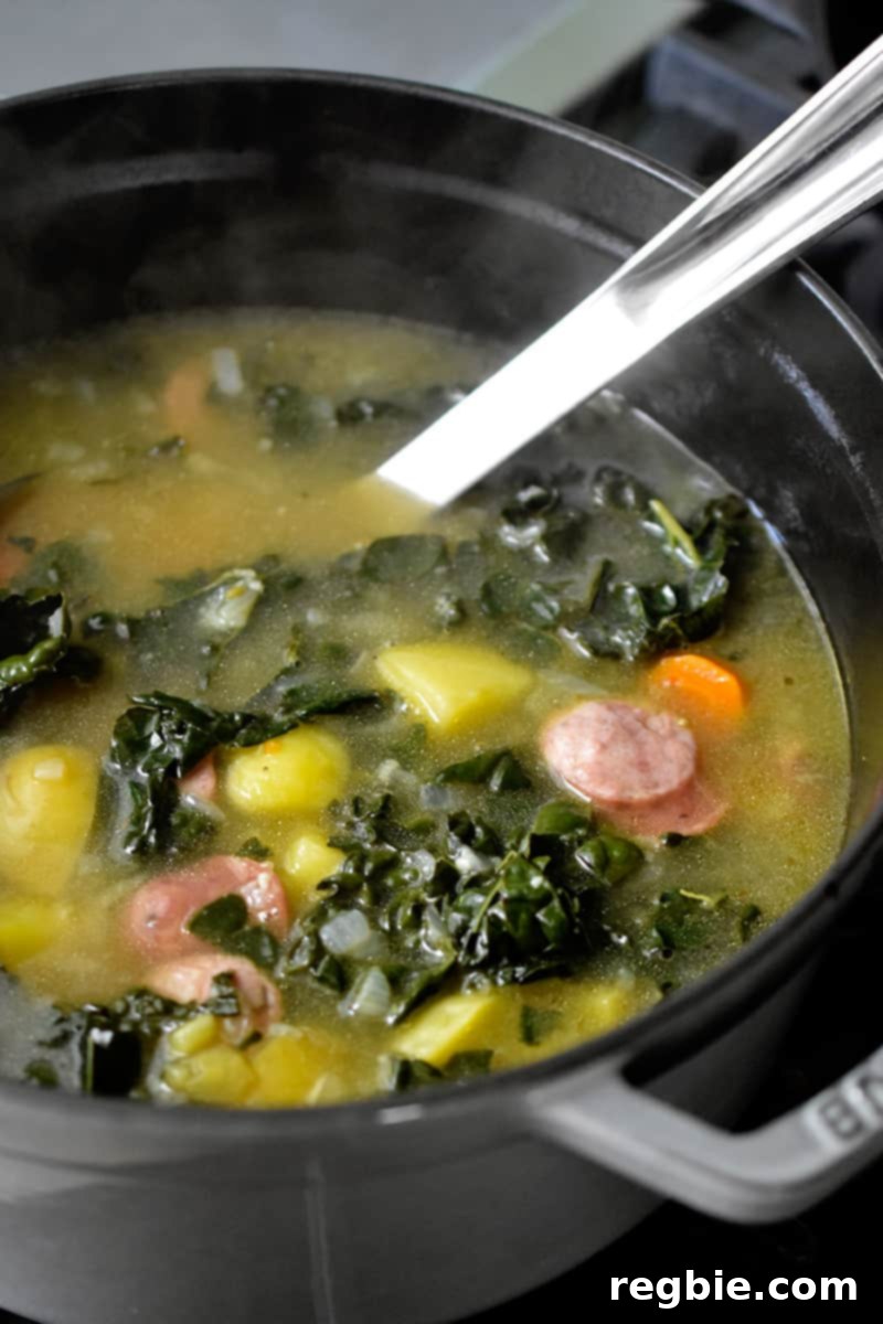 Side shot of a large pot filled with steaming hot sausage and kale soup, freshly cooked on the stovetop.