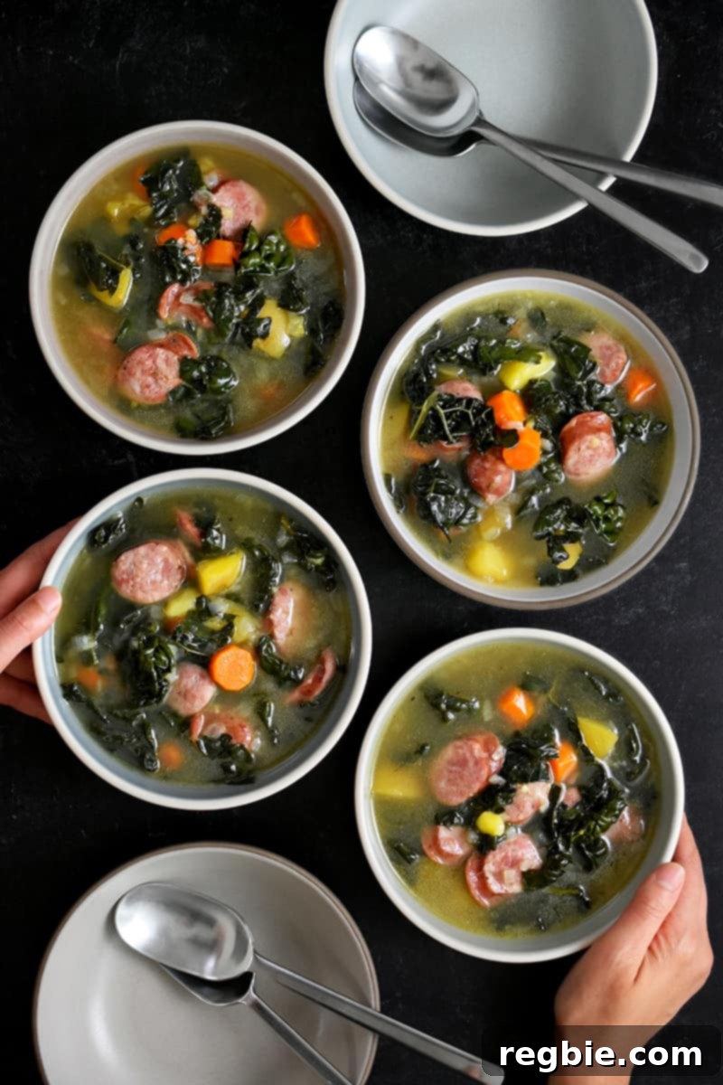 An overhead shot of a hand reaching for one of four bowls filled with delicious sausage kale soup.
