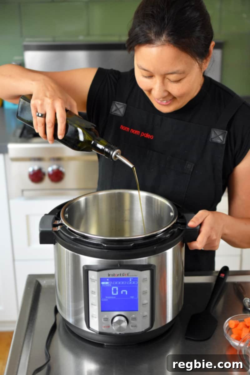 A person adding extra virgin olive oil to a hot Instant Pot on sauté mode.