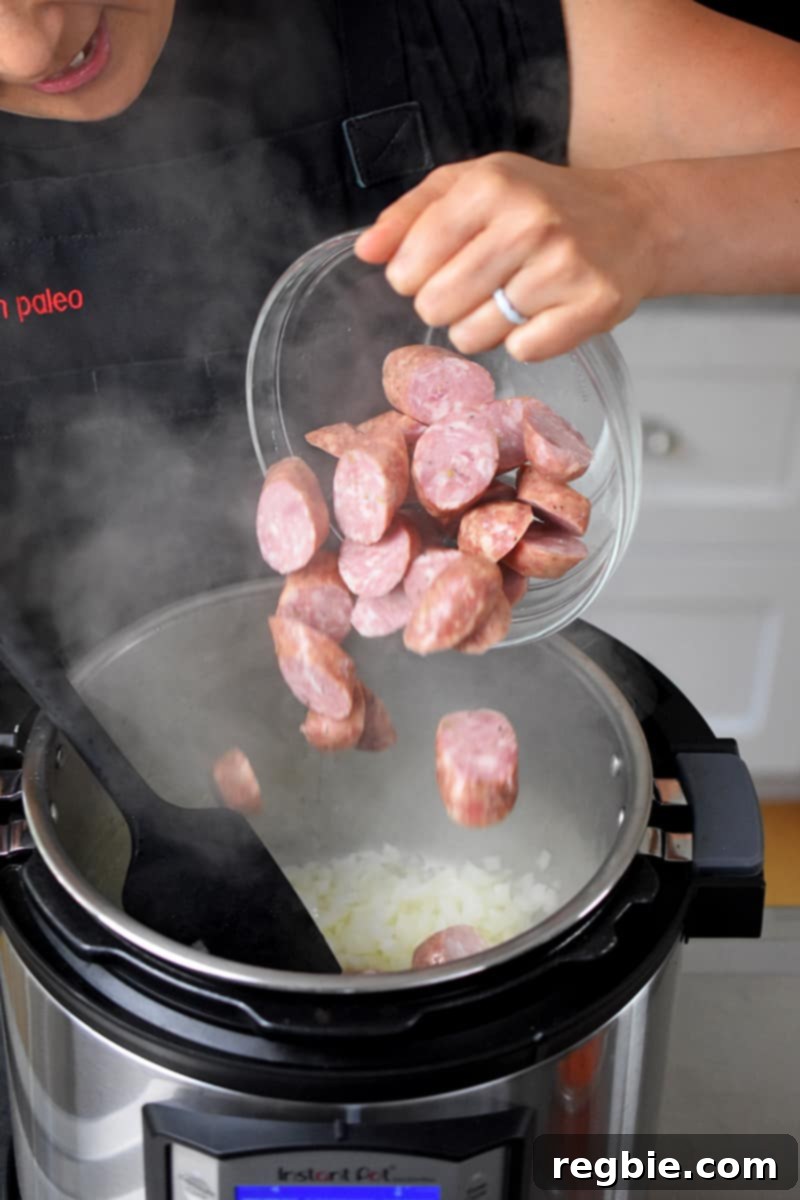 Sliced smoked sausage being added to the Instant Pot with sautéed onions.