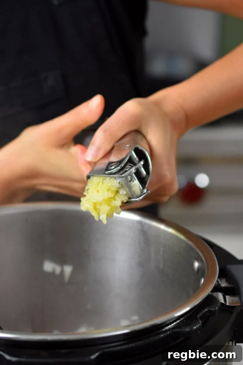 Minced garlic being added to the Instant Pot from a garlic press.