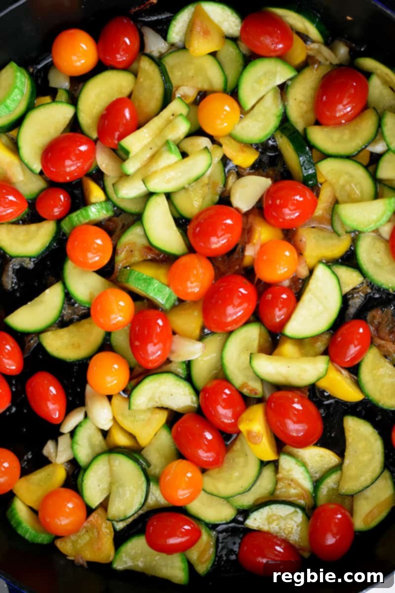 An overhead shot of a skillet filled with sautéed sliced summer squash, browned shallot slices, and cherry tomatoes
