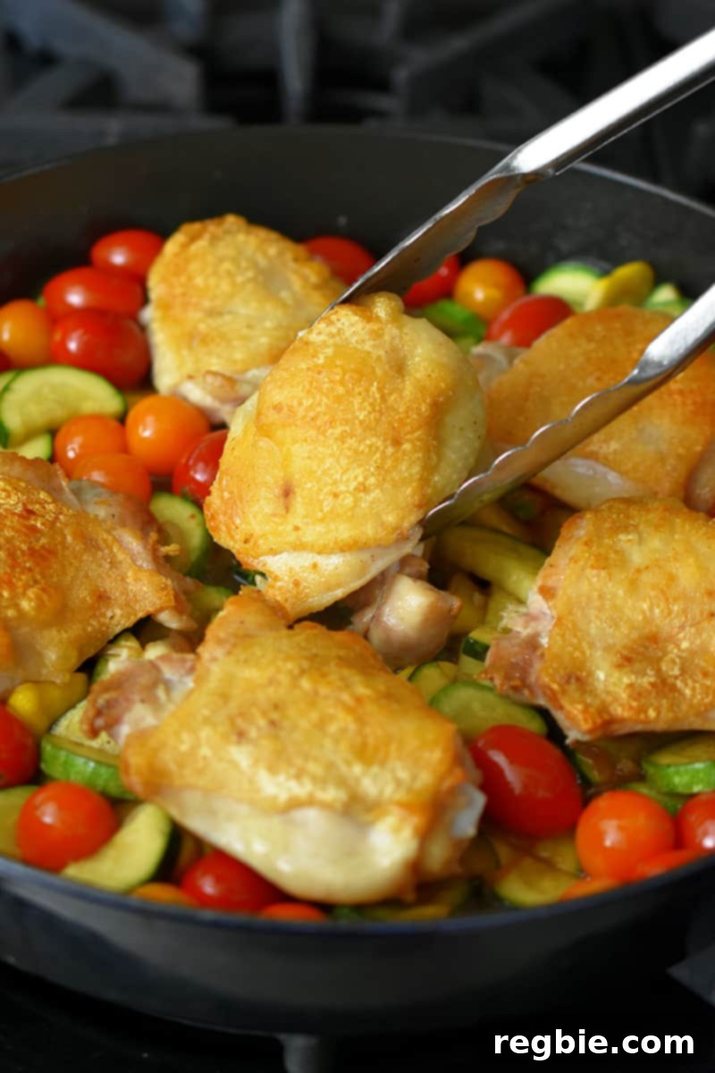 Adding crispy chicken thighs to a skillet filled with sautéed summer vegetables