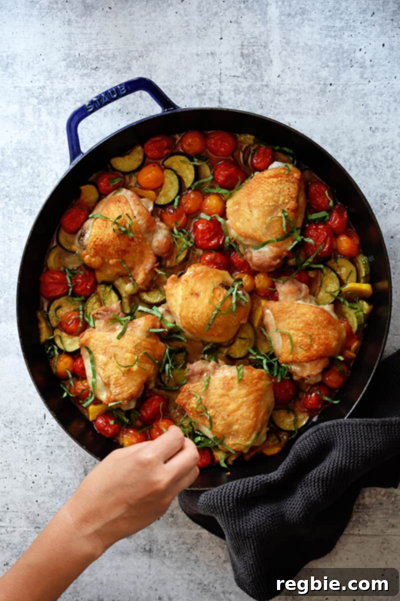 An overhead shot of crispy baked chicken thighs and summer vegetables in a skillet.
